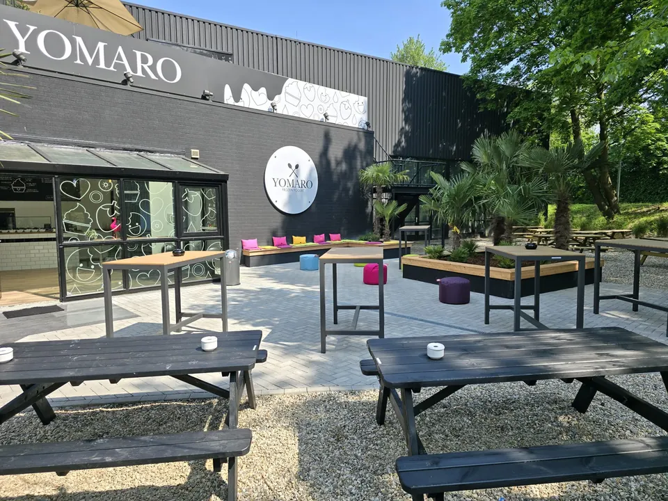 Biertischgarnituren aus dunklem Holz auf Kies vor dem YOMARO-Gebäude im Köpi Biergarten Duisburg